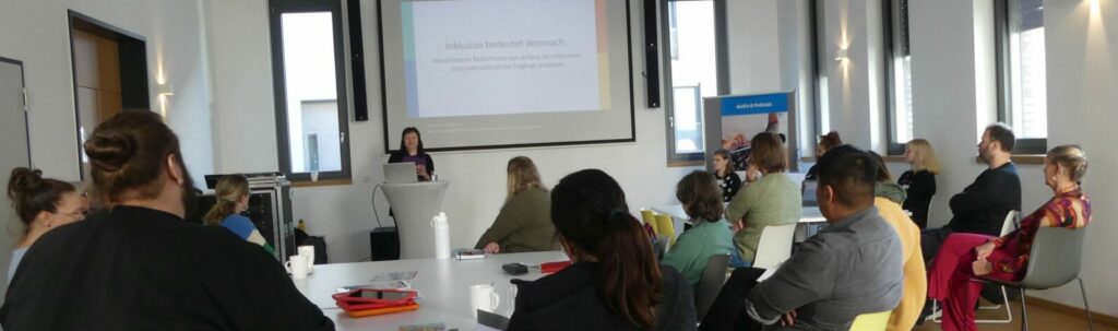 Dr. Christine Ketzer beim Vortrag zu Inklusiver Medienarbeit. Sie steht vorne an einem Pult mit Laptop. Vor ihr sitzen pädagogische Fachkräfte und hören ihrem Vortrag zu.  