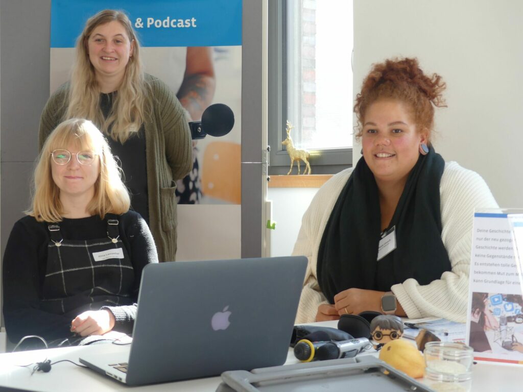 Melanie Leusch sitzt mit teilnehmenden pädagogischen Fachkräften an der Workshop Station zum Thema Audio & Podcast. 